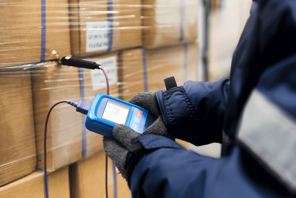 Hand of worker using thermometer to measure the temperature of goods boxes.